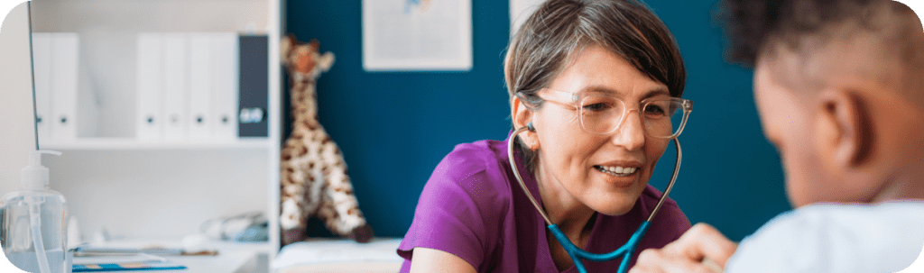 A doctor wearing a purple shirt and a blue stethoscope listening to a child's heart.