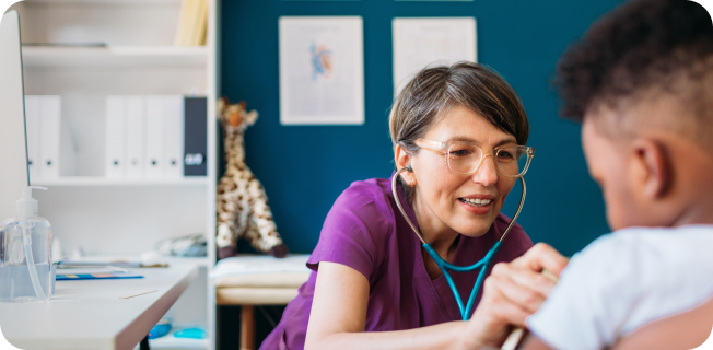 A doctor wearing a purple shirt and a blue stethoscope listening to a child's heart.