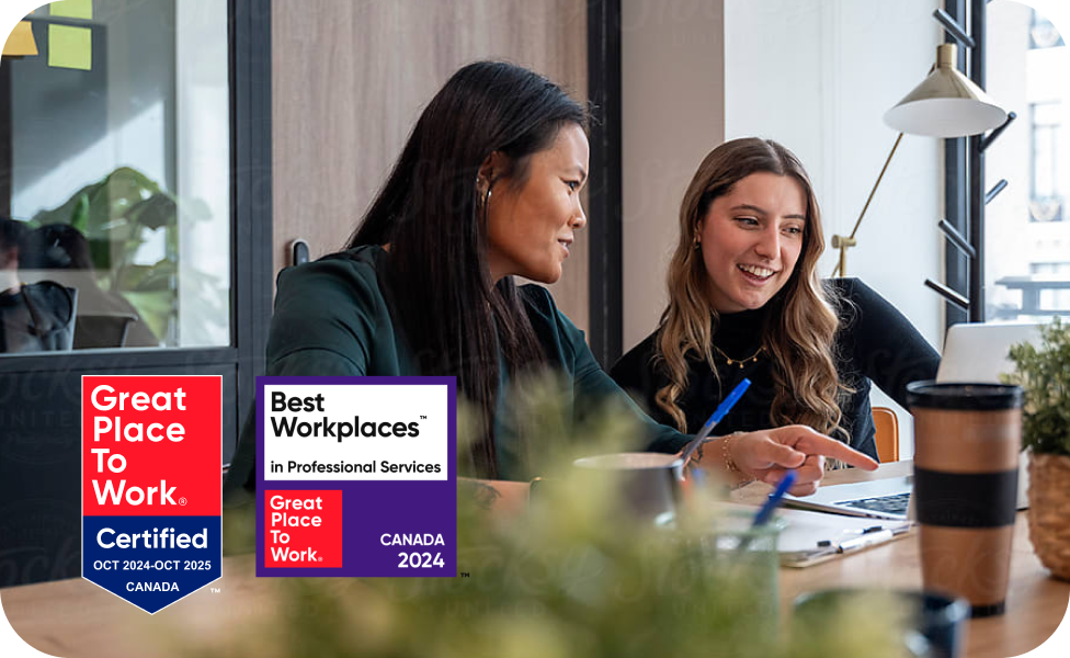 Two women in business attire sitting at a desk and pointing at a laptop. There are two badges stating Great place to Work 2024 to 2025 and Best Workplaces Canada 2024.