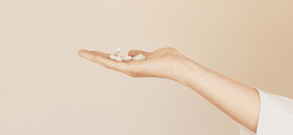 A hand holding several white pills