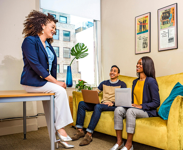 A group of three friends sitting around a bright yellow couch chatting.