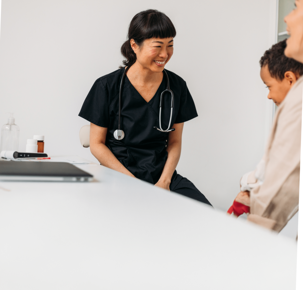 A woman in black medical scrubs wearing a black stethoscope. She's smiling as she talks to a family.