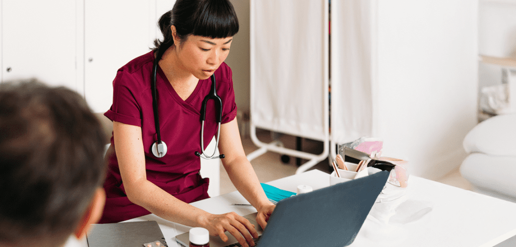 A closeup view of a woman typing on her laptop while someone in the foreground chats with her.