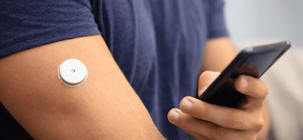 A closeup of a person's arm with a white medical device patch on their bicep.
