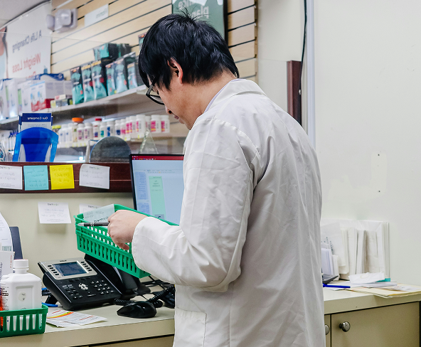 A pharmacist working behind the counter and sorting through green baskets.